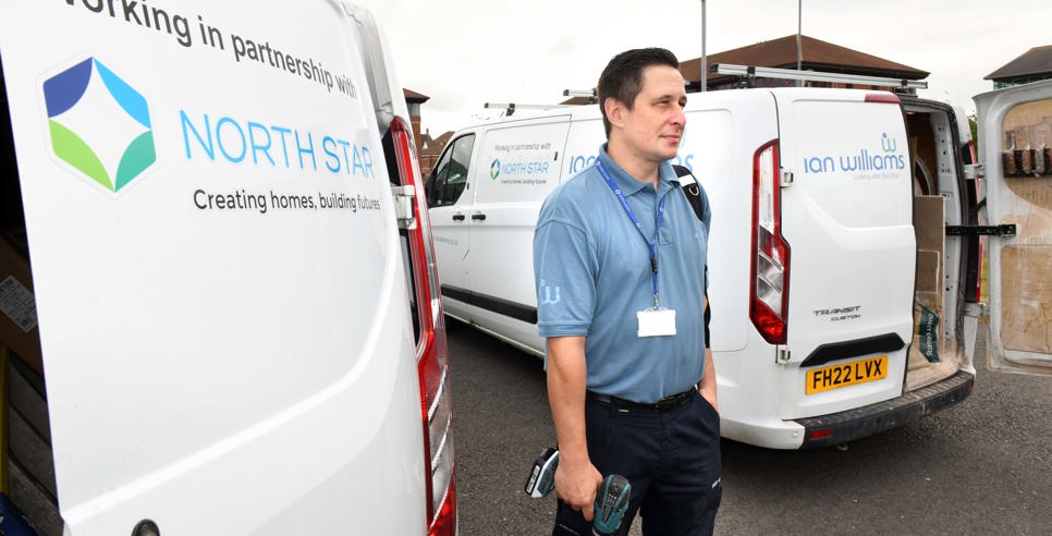 A repair worker stands between two branded vans from Ian Williams and North Star Housing. He is holding tools and wearing a blue uniform and lanyard. The vans display the logos and partnership between Ian Williams and North Star Housing.