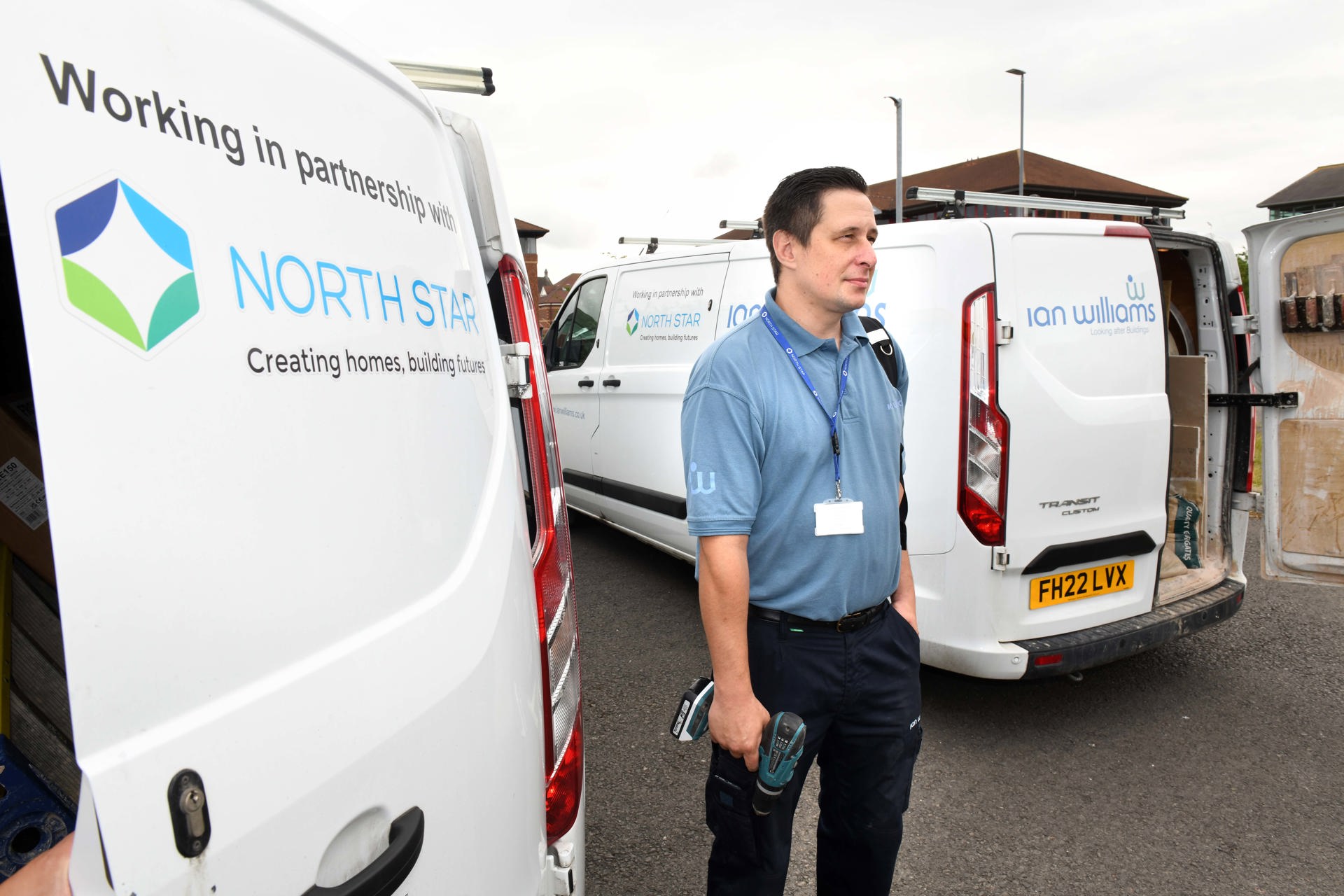 A repair worker stands between two branded vans from Ian Williams and North Star Housing. He is holding tools and wearing a blue uniform and lanyard. The vans display the logos and partnership between Ian Williams and North Star Housing.