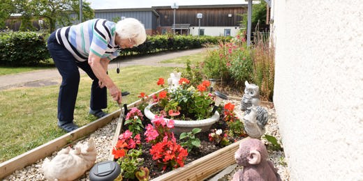 A woman tends to a flower bed surrounded by flowers and garden ornaments.