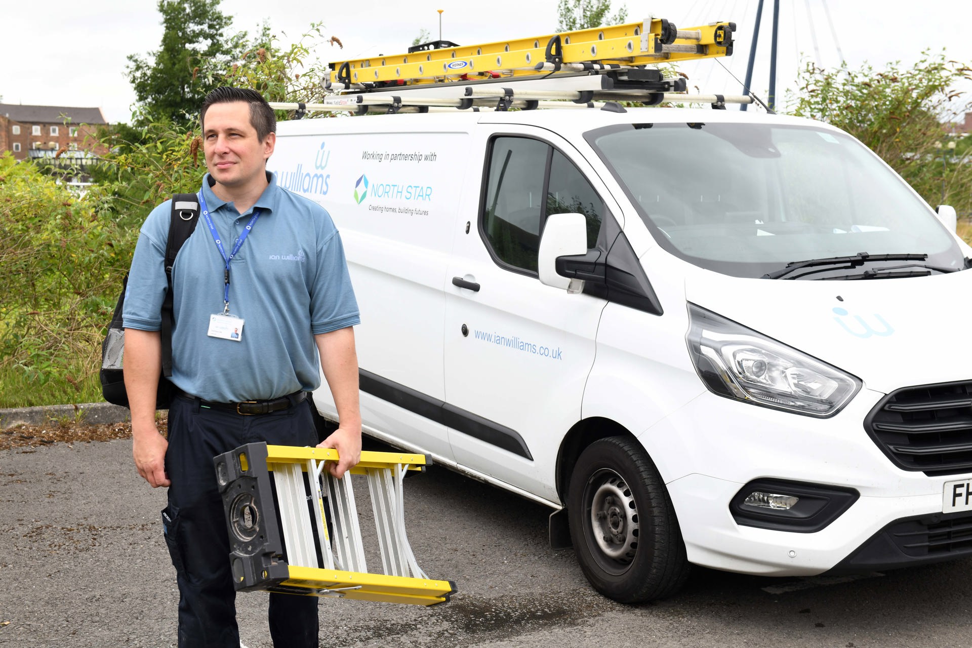 A maintenance worker from Ian Williams, carrying a ladder and a tool bag, stands beside a branded service van. The van features logos for Ian Williams and North Star Housing Group, highlighting their partnership.